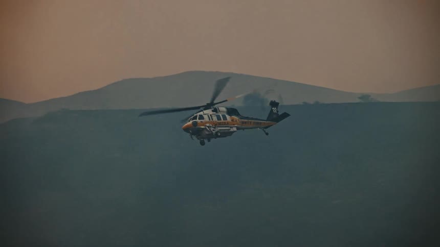 Military helicopter drops water on mountains with forests that are on fire