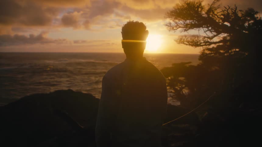 Silhouette of a person watching sunset across the ocean from atop a mountain