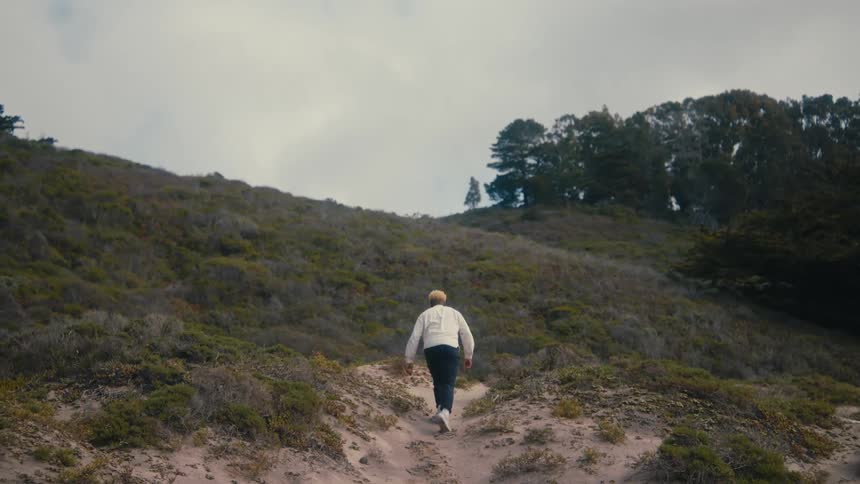 A hiker climbs a sandy hill near a forest on a cloudy afternoon