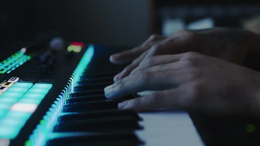 A musicians hands playing an illuminated electronic keyboard with vibrant led lights glowing in a dimly lit setting creating a futuristic and immersive atmosphere
