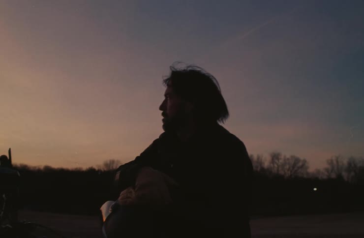 Man sitting on a motorcycle enjoying the silhouette of a landscape at dawn
