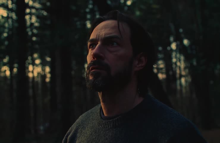 A man stands in the middle of the forest at sunset looking around with his hands extended