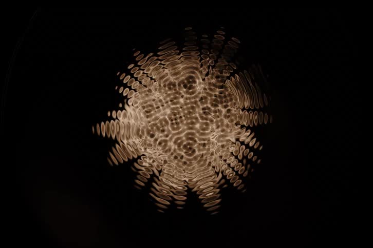 An abstract pattern of concentric circles and radiating lines glows with a warm textured light against a dark background