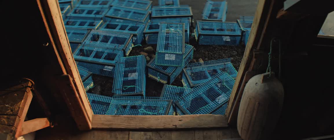 Several blue lobster traps are scattered across the shore as seen from a fishing workshop