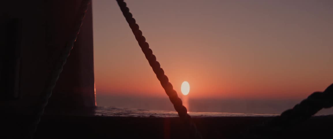 The silhouette of a rope on a fishing vessel contrasting with an orange sun on the horizon