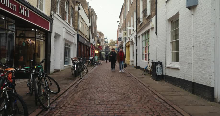 A time lapse of several people passing through a small block street with several houses around it and some parked bicycles