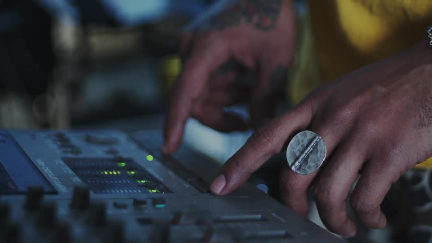 A hand wearing a bracelet is adjusting the controls on an audio mixing console