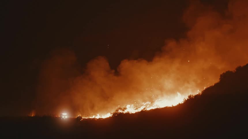 Wildfire burning aggressively across mountain ridge at night