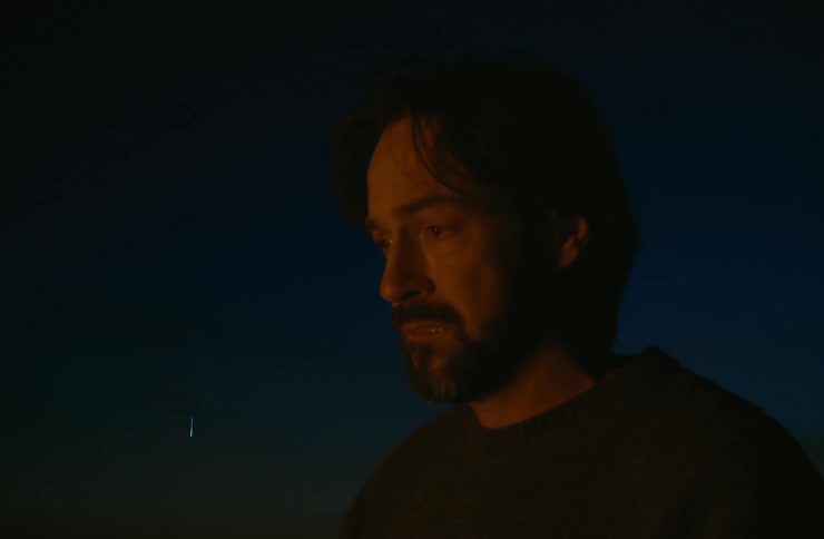 Side portrait of a bearded man in an open space at night with a fire reflection on his face