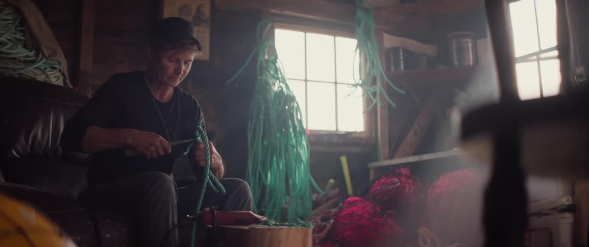 A woman sitting in her fisherman's workshop cutting rope for her lobster traps