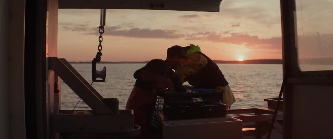 Silhouette of two fishermen taking out lobsters from a trap on a boat in the middle of the sea