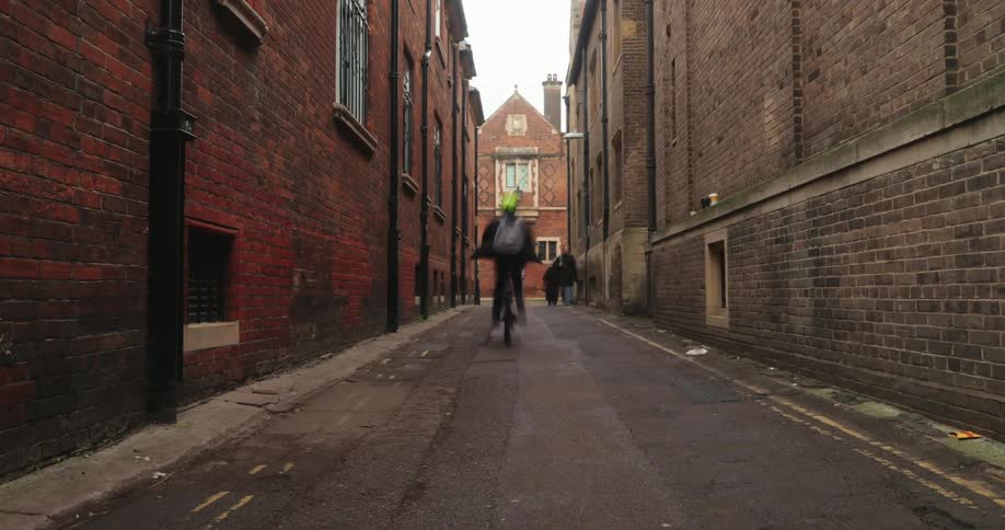 Timelapse of people walking through a narrow alleyway between brick buildings
