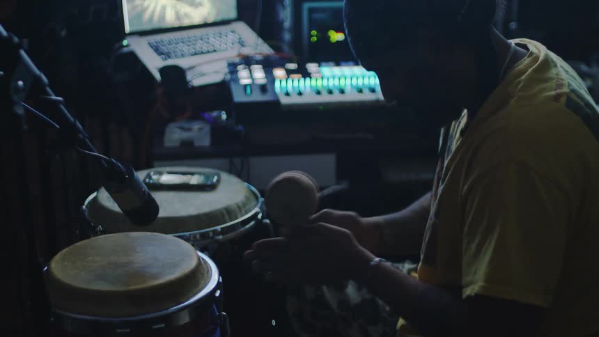 A man in a yellow shirt is in a recording studio spinning a small drum in front of a microphone