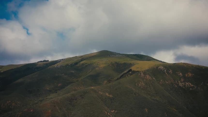 A craggy mountain peak rises against a cloudy sky with patches of green grass dotted across its rocky surface