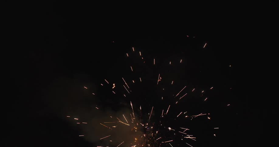 Firework mortars explode overhead scattering bright sparks and smoke against the night sky