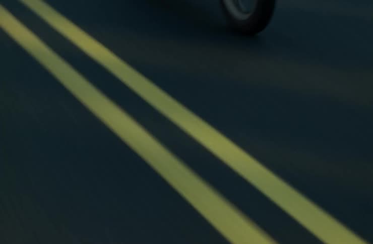 A motorcycle is being ridden on a paved road in the countryside near a forested area