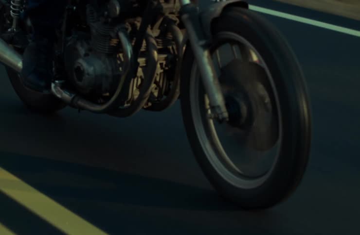 A motorcycle is captured in motion on a road with double yellow lines highlighting the front wheel and engine area