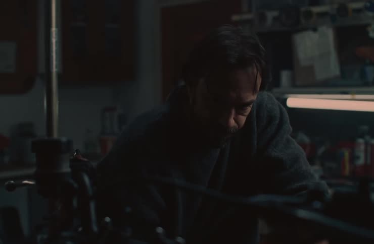 Man with a beard and a dark sweater works concentratedly in a dimly lit workshop