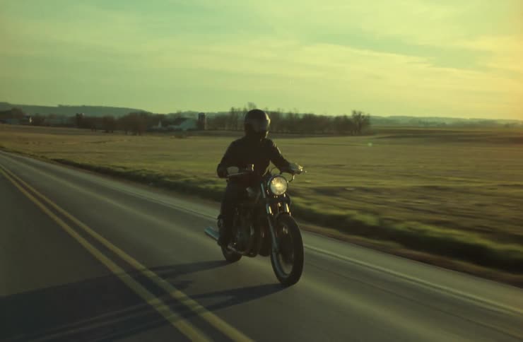 An adult is riding a motorcycle on a rural highway at sunset