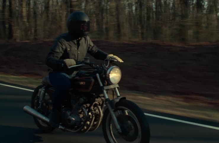 A man rides his motorcycle past the forest