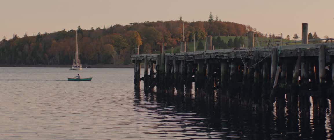 Person rowing a boat past a wooded dock on the ocean