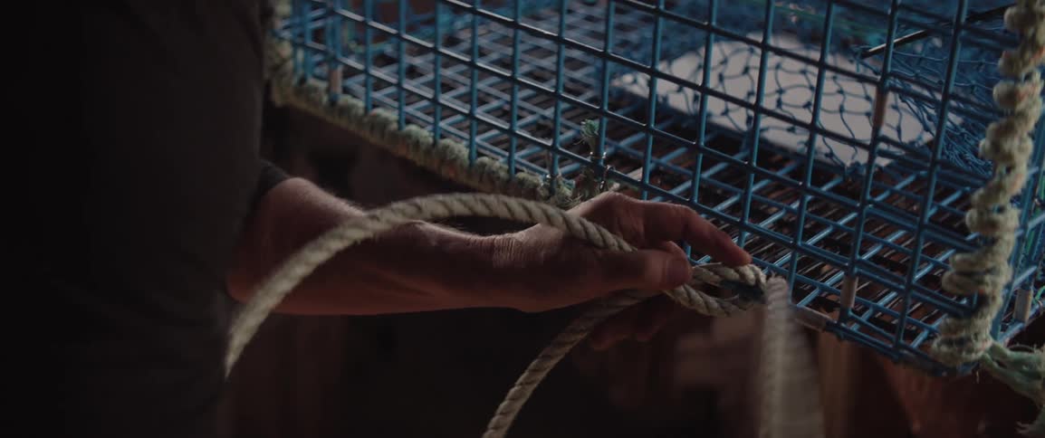 A fisherman weaving a fishing cage with rope