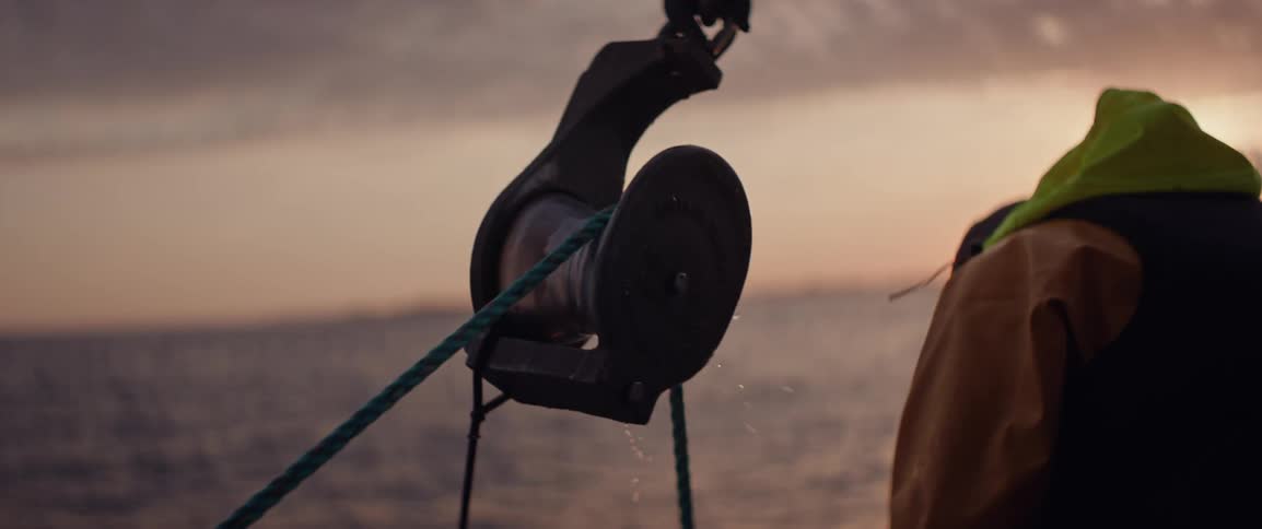 A fishing line being pulled through a pulley as a fisherman works at dawn