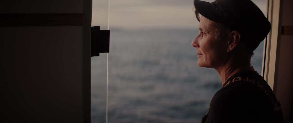 A woman gazes out the window of her fishing boat during sunrise