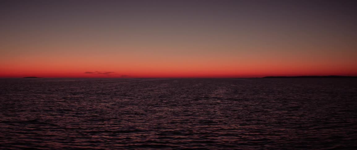 Seascape of calm ocean with reddish sky on the horizon at dawn
