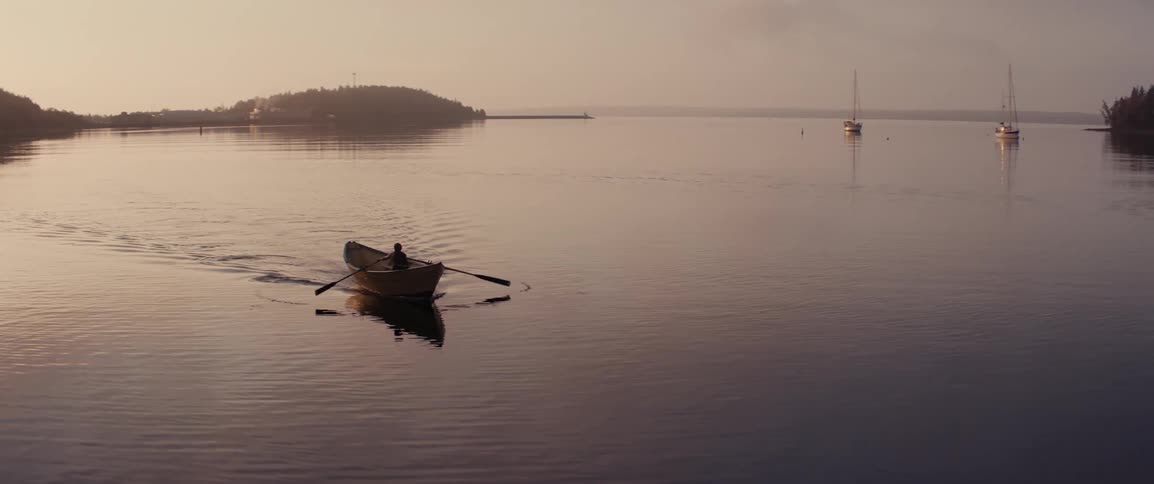 Silhouette of a person rowing a small wooden boat at dawn
