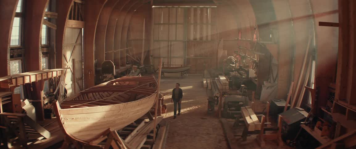 Woman walking in a boat building workshop towards a row boat