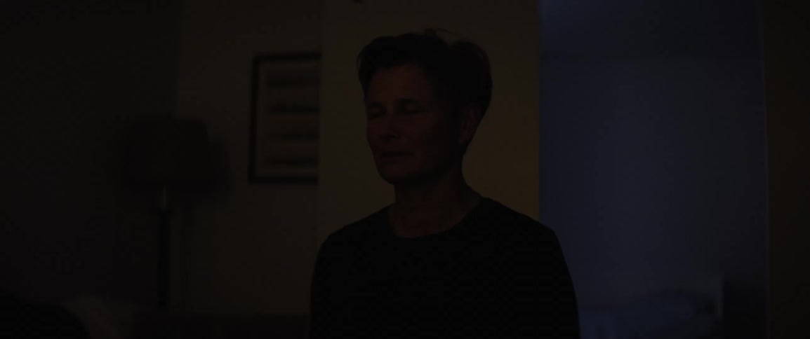 Closeup of the face of a woman sitting in a room at night with bright lights entering from the window
