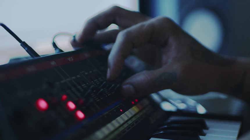 Hand adjusts the controls of an analog synthesizer with red lights on
