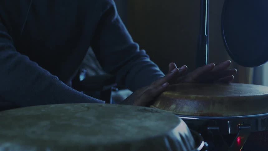 A person is playing a set of hand drums in a dimly lit room