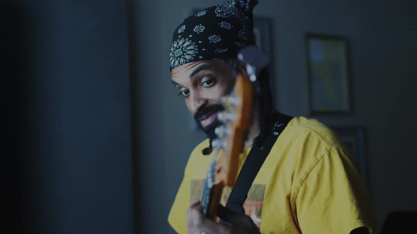 Bearded man wearing a black bandana and a yellow tshirt plays an electric bass guitar