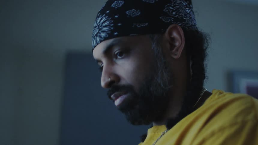 A man wearing a bandana bobs his head while listening to music at home