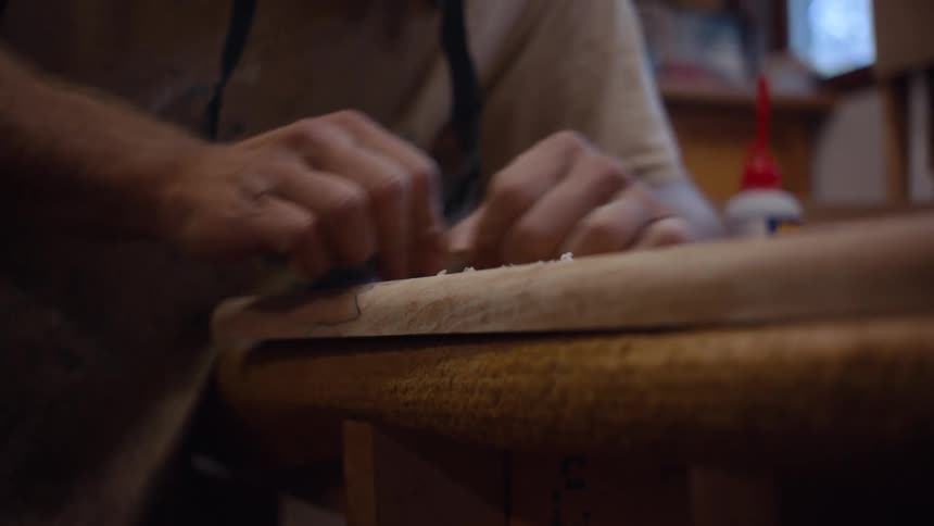 Hands working on a piece of wood with wood shavings scattered on the surface