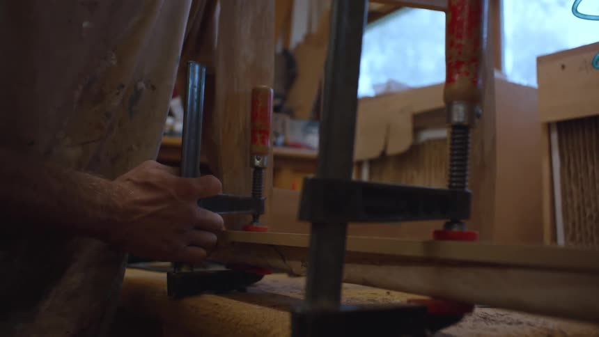 Hands of a man tightening a carpentry clamp on a piece of wood inside a workshop