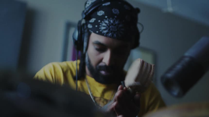 A man wearing headphones and a bandana on his head is spinning a small drum in front of a microphone