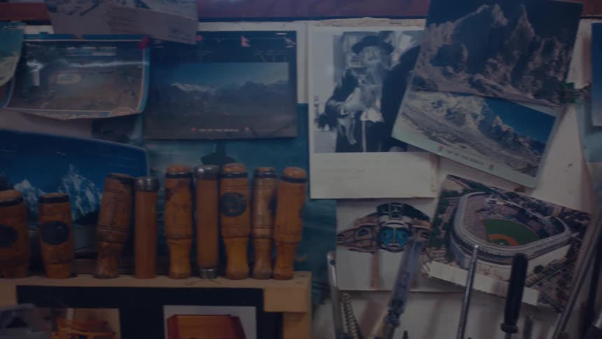 A cluttered wall displays various photographs postcards and tools including a row of woodenhandled implements