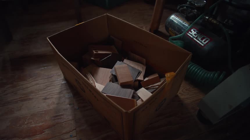 A cardboard box is filled with assorted wood pieces of varying sizes and shapes likely scraps or offcuts from a woodworking project