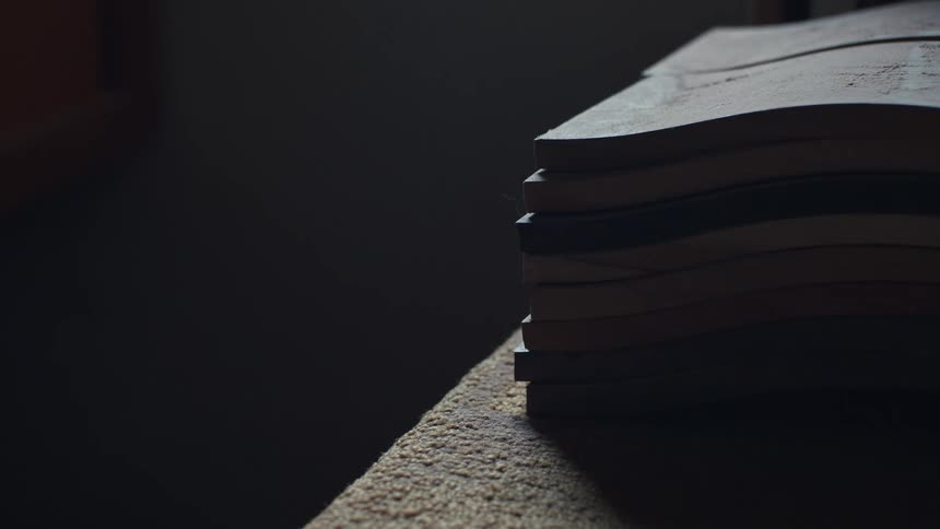 A neat stack of wooden boards sits on a table in a dimly lit workshop