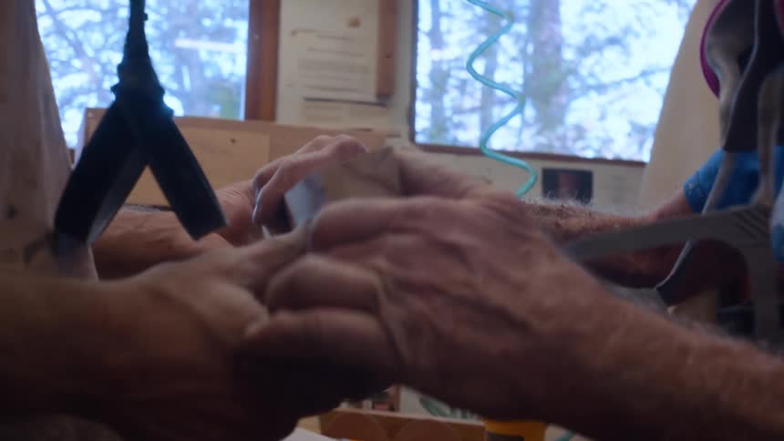 Two people work together in a workshop inspecting a piece of wood in front of a workbench
