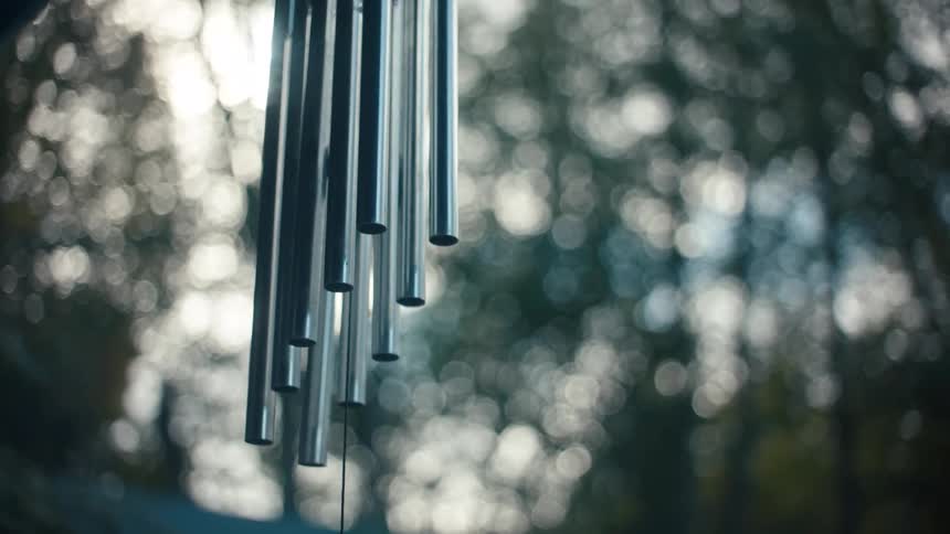 Metal tubes of a wind chime hang against a blurred background of trees