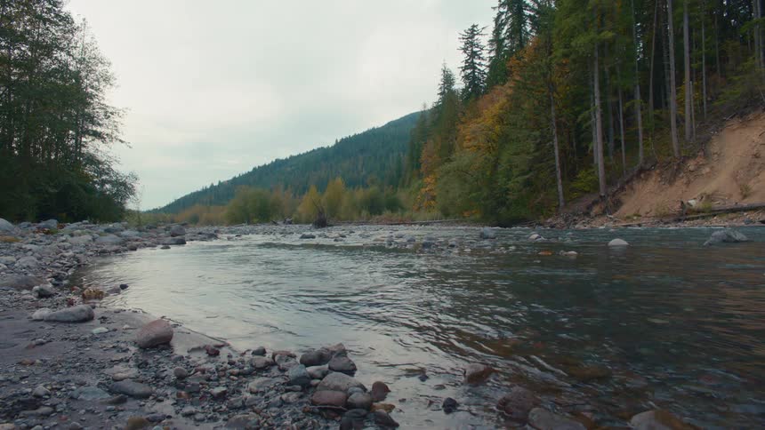 A gently flowing river winds through a forested valley flanked by rocky shores and autumn foliage on the mountain slopes
