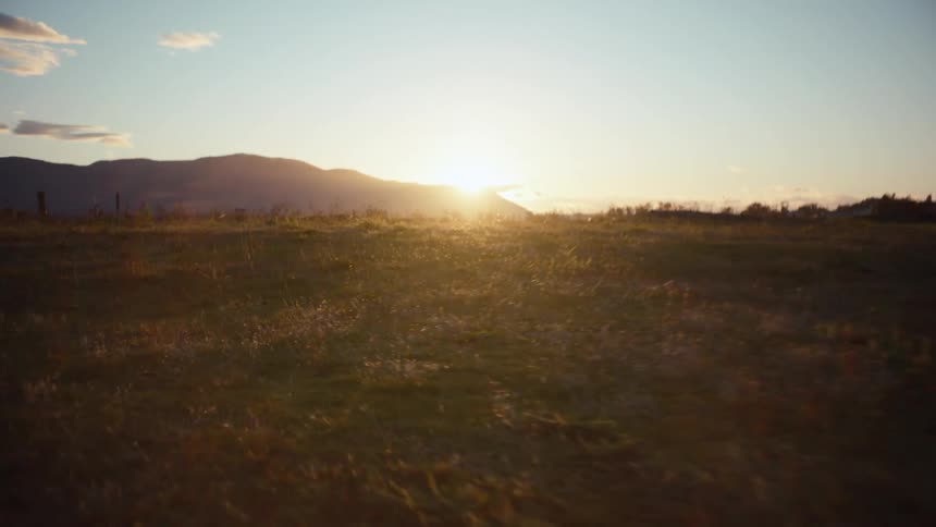 Running up a sunlit field at sunset with a mountain range partially covering the glowing horizon