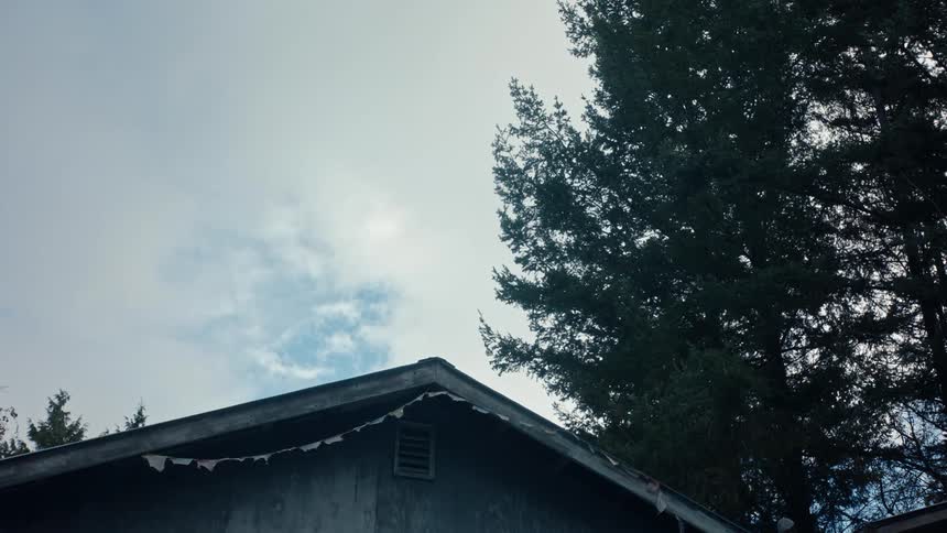 A slight breeze rustles the tree branches and house decorations while clouds drift overhead