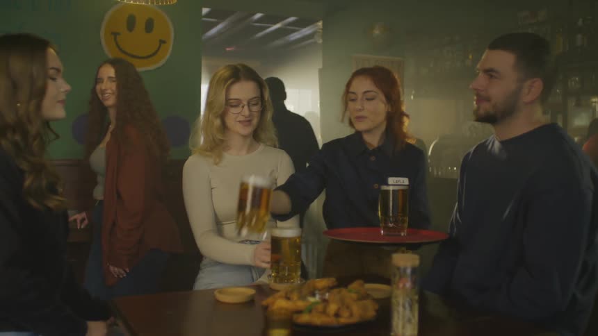 Waiter delivering beers to friends toasting while sitting at a bar table