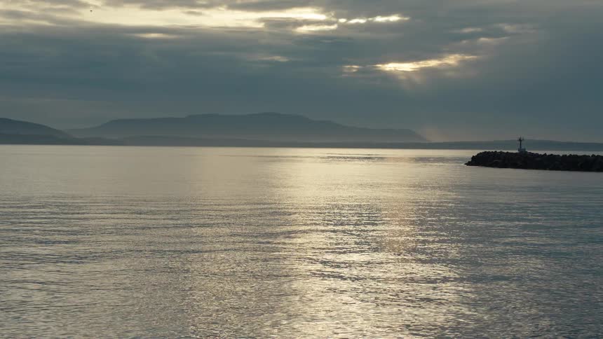 Rays of sunlight pierce through dark clouds and reflect on the calm surface of the sea