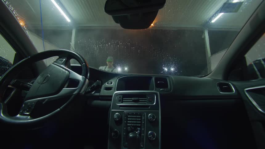 Interior view from inside car of windshield getting hosed off at carwash by an employee